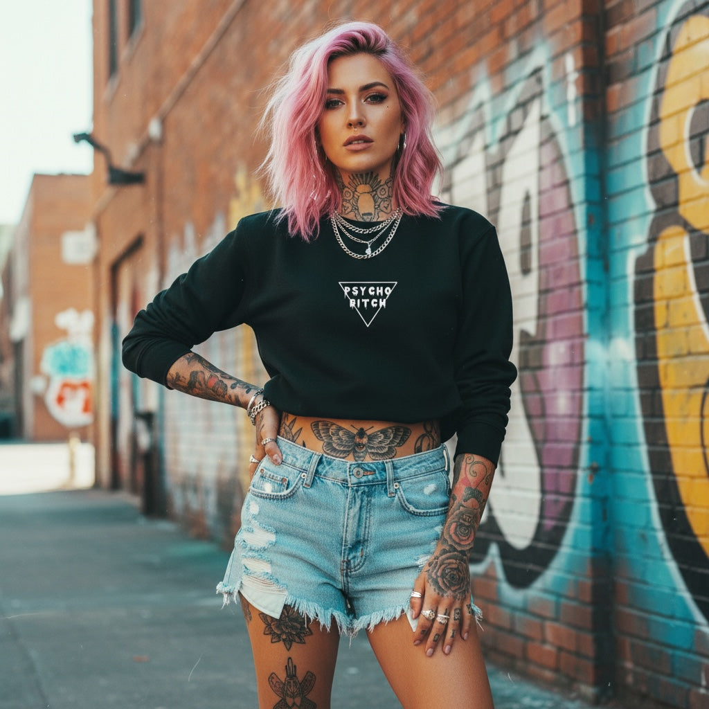 A model with pink hair wears a black oversized crewneck flaunting bold 'PSYCHO BITCH' text against a graffiti backdrop.