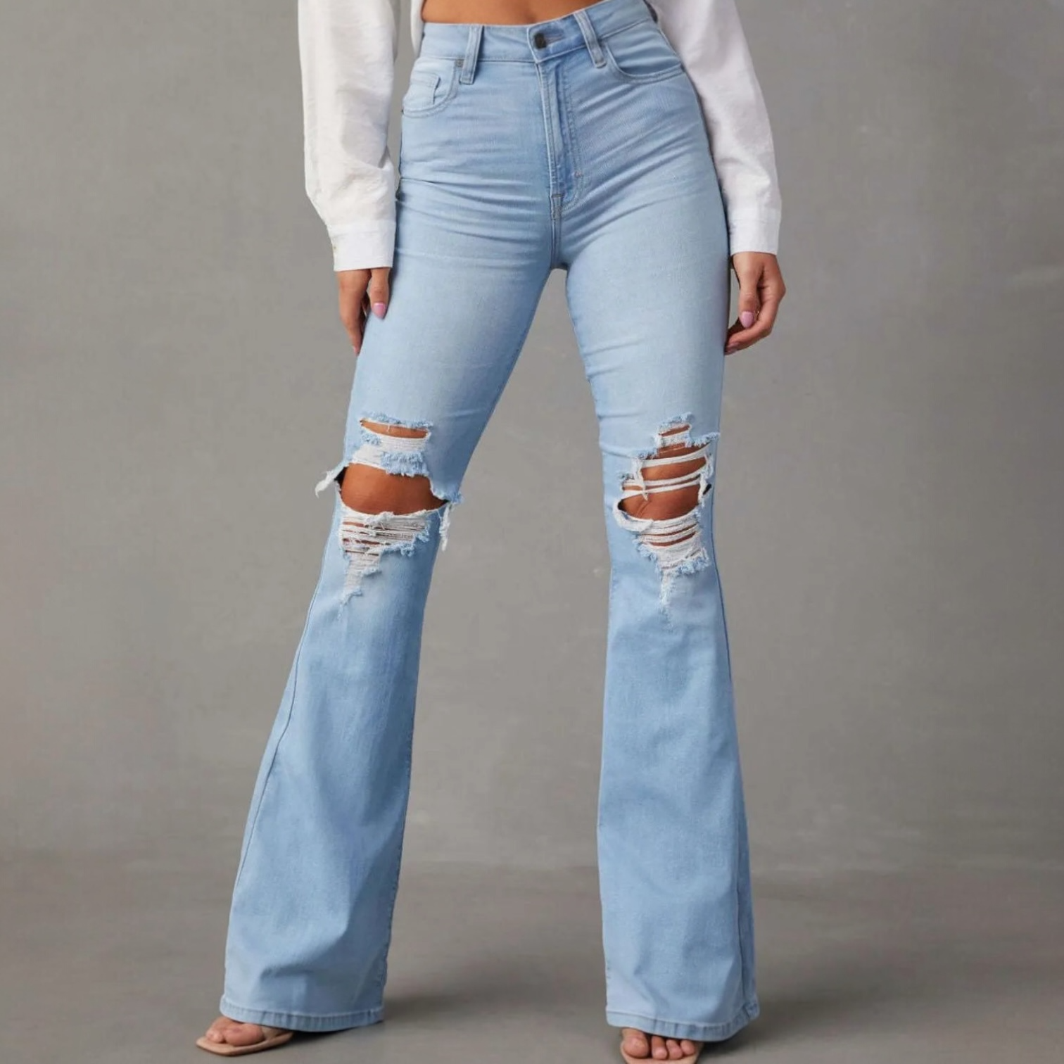 Light wash distressed flare jeans with rips at the knees, styled with a fitted top for a bold look.