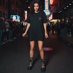 A scallywag in a black oversized tee with a chest logo and bold back graphic, set against a bright urban backdrop.