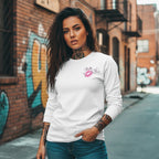 A white long sleeve shirt with bold graphics, worn by a model against a graffiti-covered brick wall.