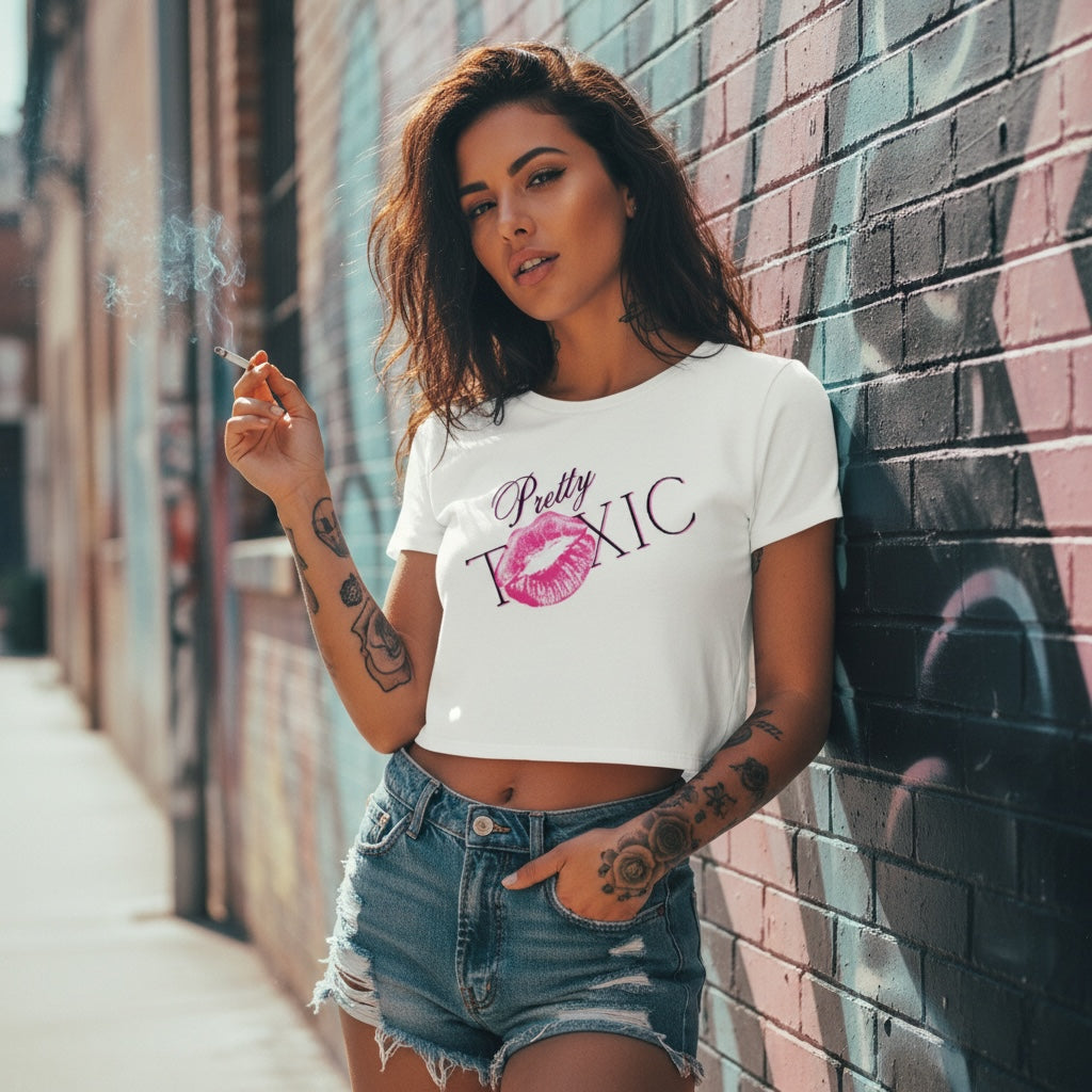 A woman in a fitted white cropped tee with a bold 'Pretty Toxic' graphic, holdin' a cigarette against a brick wall.