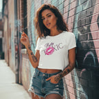 A woman in a fitted white cropped tee with a bold 'Pretty Toxic' graphic, holdin' a cigarette against a brick wall.